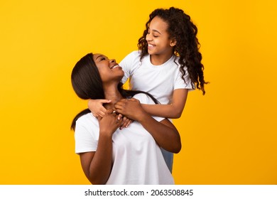 Mother Daughter Bonding Concept. Portrait of cute black girl and her smiling mom hugging and looking to each other's eyes, isolated on yellow orange studio background. Healthy United Family
