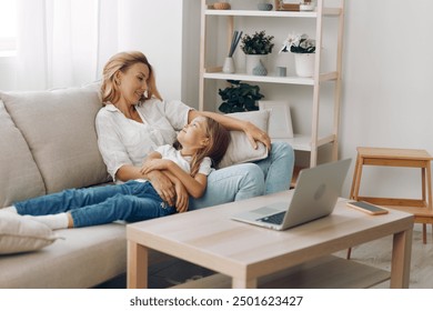 Mother and daughter bonding on the couch with a laptop and a bookshelf filled with books in the background - Powered by Shutterstock