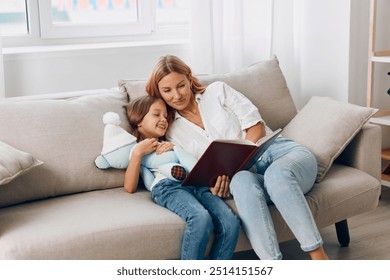 Mother and daughter bonding on the couch, reading a book together while cuddling a stuffed animal - Powered by Shutterstock