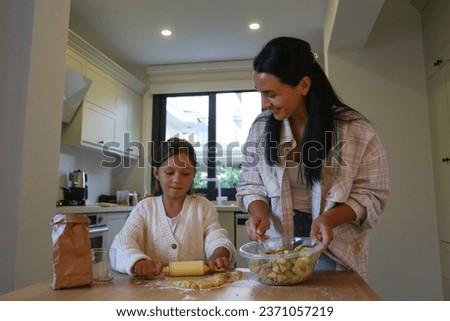 Mother and daughter bonding through cooking together a traditional apple pie for thanksgiving. Little girl helping her mom to prepare food. Close up, copy space, kitchen background.