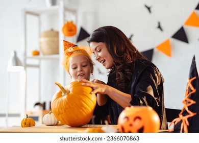 Mother and daughter carving pumpkin for Halloween autumn holidays. Mother and daughter in costumes decorating the home and having fun. - Powered by Shutterstock