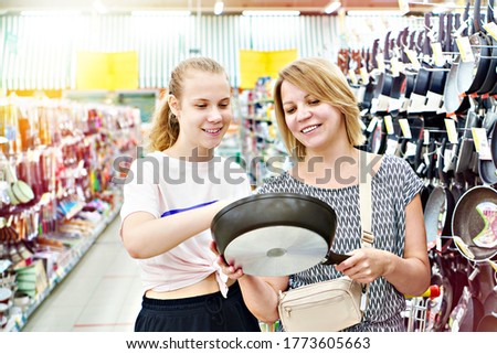 Mother and daughter choose a frying pan in a supermarket