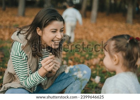 Mother and daughter collecting wild flowers in autumn forest. Young mother and her little daughter together