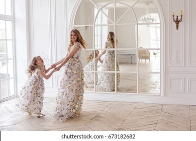 Mother And Daughter Dancing In The Mirror In The Same Dress In A Big White Room