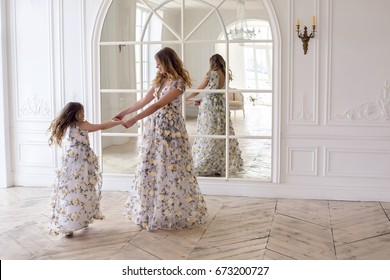 Mother And Daughter Dancing In The Mirror In The Same Dress In A Big White Room