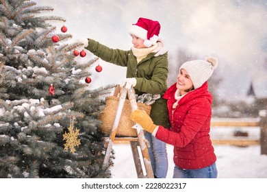 mother and daughter decorate a Christmas tree snowy winter outside