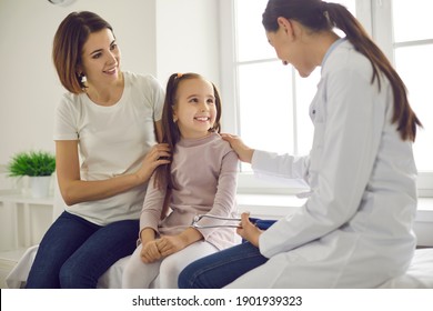 Mother And Daughter At The Doctor's Office. Friendly Female Practitioner Talking To Child During Health Checkup At The Clinic. Happy Little Patient Smiling At Pediatrician During Visit To The Hospital