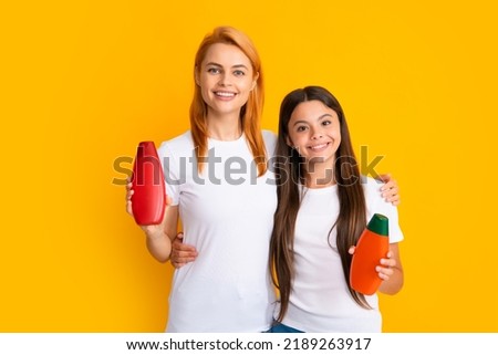 Mother and daughter doing morning hair care. Smiling mom and kid in show clean mockup shampoo, conditioner or face wash bottles. Children and adults dermatology products.