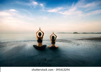 Mother And Daughter Doing Yoga At Beach