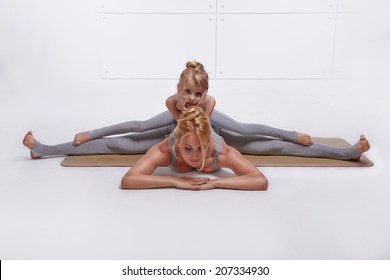 Mother Daughter Doing Yoga Exercise,fitness Family Sports, Sports Paired Woman Sitting On The Floor Stretching His Legs Apart In Different Directions Pose Child Sits On Top Of The Twine In  Same Pose