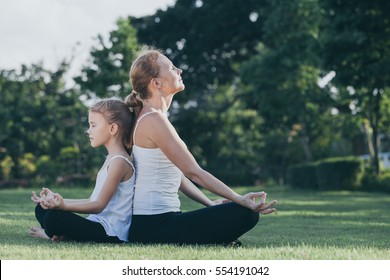 Mother and daughter doing yoga exercises on grass in the park at the day time. People having fun outdoors. Concept of friendly family and of summer vacation. - Powered by Shutterstock