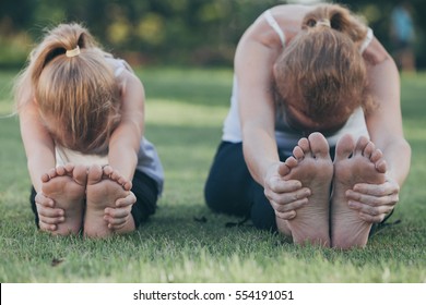 Mother and daughter doing yoga exercises on grass in the park at the day time. People having fun outdoors. Concept of friendly family and of summer vacation. - Powered by Shutterstock