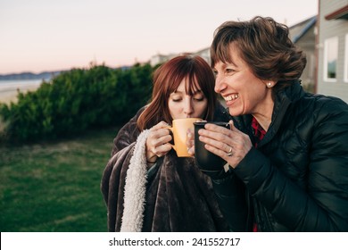 Mãe e filha bebendo de copos de café no pôr do sol na praia rindo