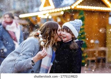 Mother and daughter eating white chocolate covered fruits and strawberry on skewer on traditional German Christmas market. Happy girl and woman on traditional family market in Germany during snowy day