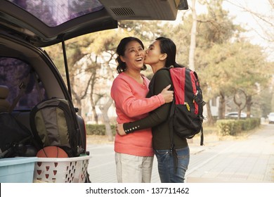 Mother And Daughter Embracing Behind Car On College Campus