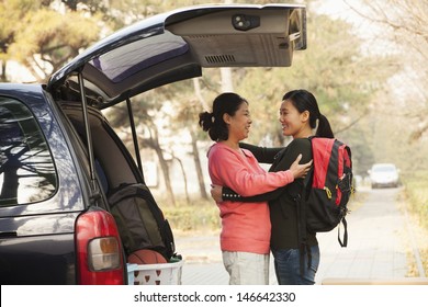 Mother And Daughter Embracing Behind Car On College Campus