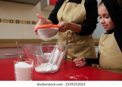 A mother and daughter enjoy a bonding moment while baking in their home kitchen. The warm atmosphere highlights family togetherness as they sift flour into a mixing bowl, sharing smiles. - Powered by Shutterstock