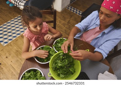 A mother and daughter enjoy quality time in the kitchen, preparing fresh leafy greens together, fostering family bonding and healthy eating habits in a cozy home setting. - Powered by Shutterstock