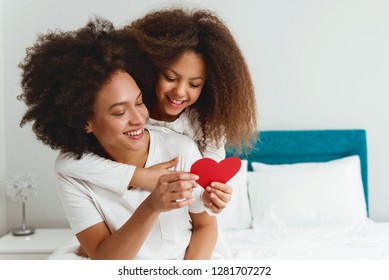 Mother and daughter enjoying on the bed, holding red hearts  - Shutterstock ID 1281707272