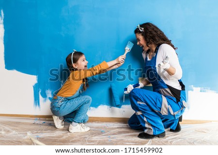 Mother and daughter enjoying together while painting wall.