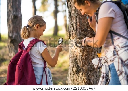 Mother and daughter  explore with magnifying glass nature while hiking.