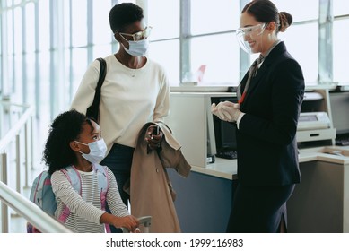 Mother And Daughter With Face Masks Passing By Airport Check-in Counter With Airport Staff Wearing Face Shield. Family Of Two Traveling During Pandemic.