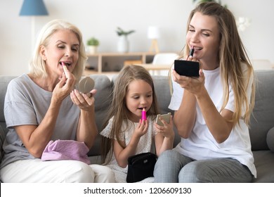 Mother, daughter and grandmother spend time at home together having fun putting make up on, three female generations enjoy sweet moments painting lips with lipsticks. Family relations concept