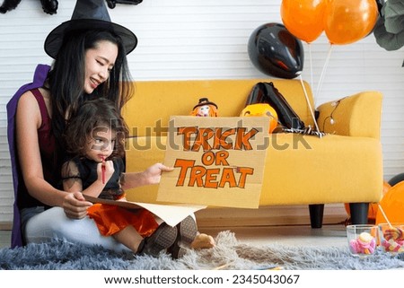 Mother and daughter in halloween costume for party, mother show trick or treat cardboard banner for her daughter, happy halloween together