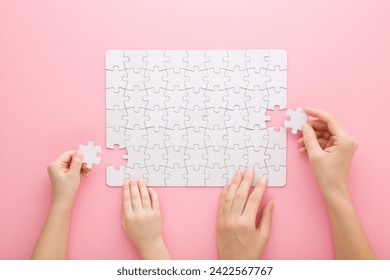 Mother and daughter hands playing and assembling white puzzle pieces on light pink table background. Pastel color. Family activities. Spending time together. Closeup. Point of view shot. - Powered by Shutterstock