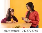 A MOTHER AND DAUGHTER HAPPILY LOOKING AT EACH OTHER WHILE HAVING BREAKFAST
