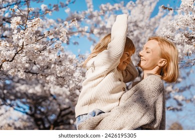 Mother and daughter are happy together in blooming trees garden at spring in sunlight. Woman mom and girl playing, dancing and hugging outdoors. Happy mother's day! Family holiday and togetherness.