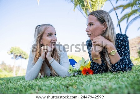 Mother and daughter are having a conversation while laying on the grass.