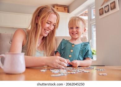 Mother And Daughter Having Fun Sitting At Table At Home Doing Jigsaw Puzzle Together