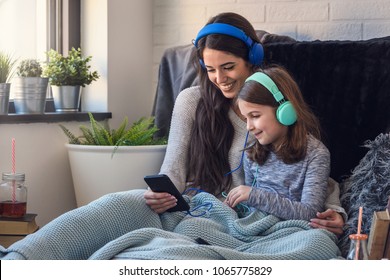 Mother and daughter having fun with smart phone and headphones. Family quality time - Powered by Shutterstock