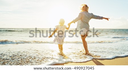 Mother and daughter having fun walking and playing on the beach at sunset