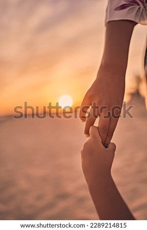 Mother and daughter holding hands with love and the sunset on the background                  