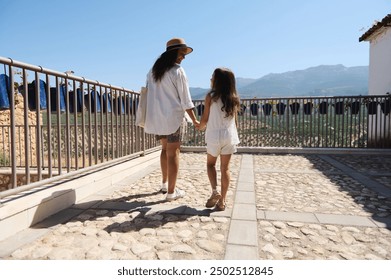 Mother and daughter holding hands, walking together on a sunny day in a picturesque location - Powered by Shutterstock