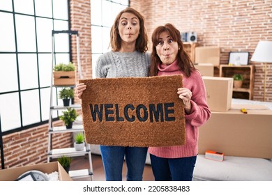 Mother and daughter holding welcome doormat making fish face with mouth and squinting eyes, crazy and comical.  - Shutterstock ID 2205838483