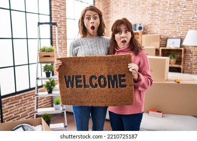 Mother and daughter holding welcome doormat afraid and shocked with surprise and amazed expression, fear and excited face.  - Shutterstock ID 2210725187