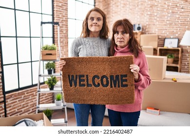 Mother And Daughter Holding Welcome Doormat Skeptic And Nervous, Frowning Upset Because Of Problem. Negative Person. 