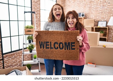 Mother and daughter holding welcome doormat smiling and laughing hard out loud because funny crazy joke.  - Shutterstock ID 2233015513