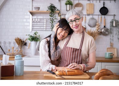 Mother And Daughter Hugging Each Other In Kitchen.Cook Bread Before The Celebration Christmas Eve Women's Day Family Love.Attractive Looking Asians Old People With Tattoos Making French,Baguette,bread