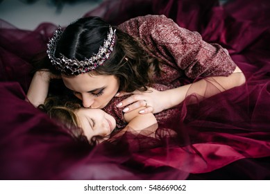 Mother And Daughter In The Image Of The Queen And Princess Dresses Color Marsala Lie Together In Bed, Close-up, Selective Focus