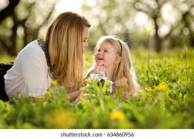 Mother with daughter a little blond girl, lying in the garden or park on the grass with flowers, love, family, communication