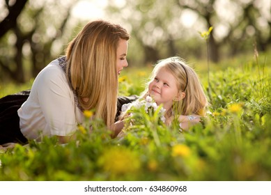 Mother with daughter a little blond girl, lying in the garden or park on the grass with flowers, love, family, communication