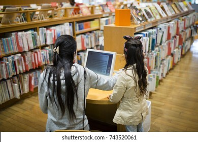 Mother And Daughter Looking For Books Using A Personal Computer