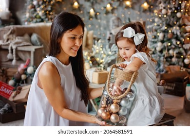 Mother and daughter are looking at Christmas decorations gold, silver and brown Christmas balls. They take it out of a large glass jar.