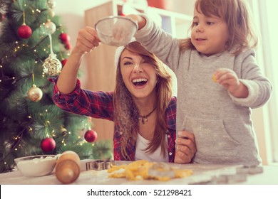 Mother and daughter making Christmas cookies and having fun. Mother sifts the flour through a sieve while daughter puts more flour in it. Focus on the mother - Powered by Shutterstock