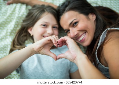 Mother And Daughter Making Heart Shape From Hand While Lying On Bed At Home