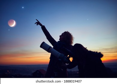 Mother and daughter observing stars, planets, Moon and night sky with astronomical telescope.